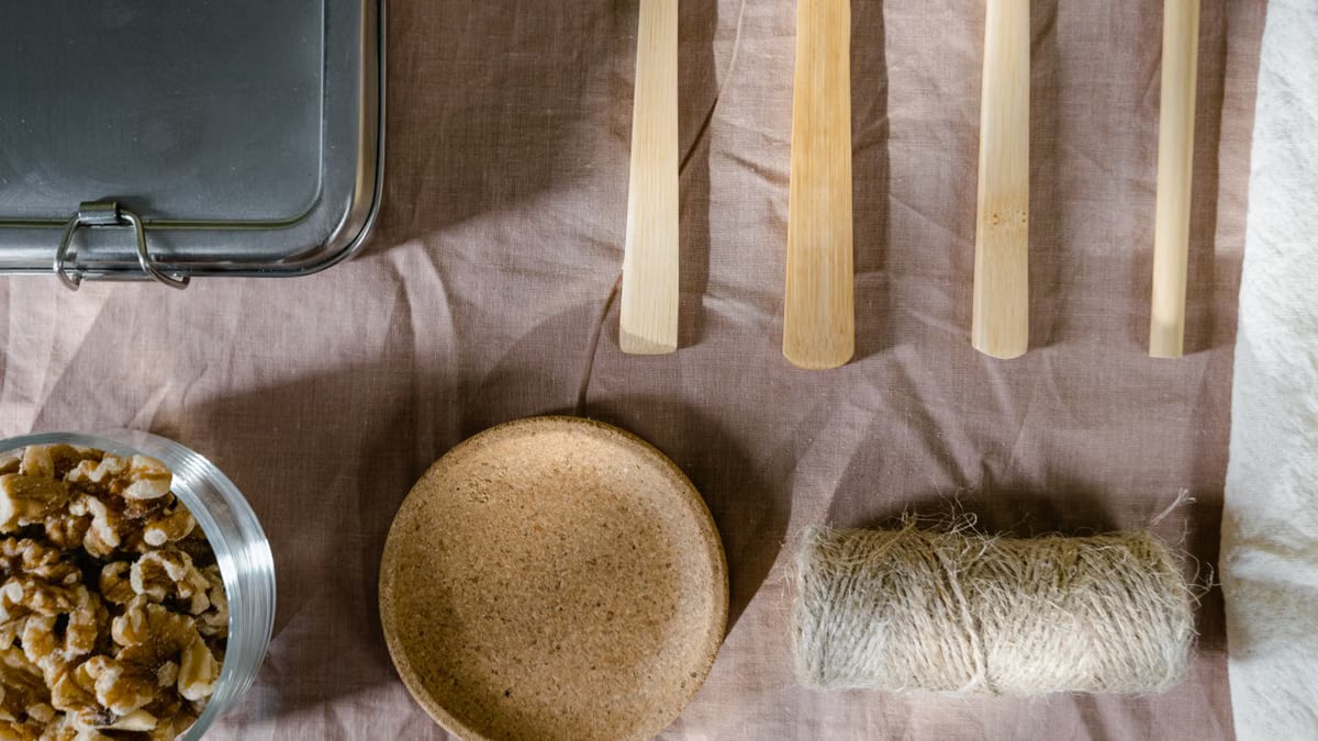 Flat lay of rustic kitchen elements including wooden utensils, nuts, and twine on cloth.